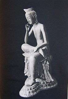Three-quarter view of a seated statue in half-lotus position. The right foot rests on the left upper leg, the right elbow rests on the right knee with the right hand close to the head in contemplating pose.