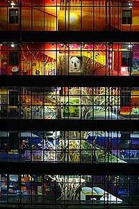 An illuminated, colorful mural painting distributed across the galleries and interior staircase along the five-floor facade of the interior courtyard of an office building