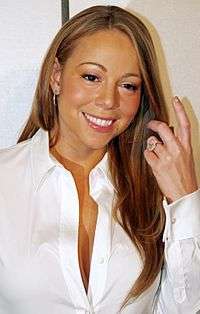 A light haired medium skin colored female smiling. The female has long hair and is wearing a white sleeved shirt that is slightly un-buttoned at the top.