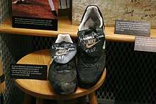 Dark baseball cleats with the NIKE brand name bearing the silver signature "Mariano Rivera MVP" sit on a wooden stool