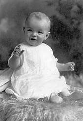 Monroe as an infant, wearing a white dress and sitting on a sheepskin rug