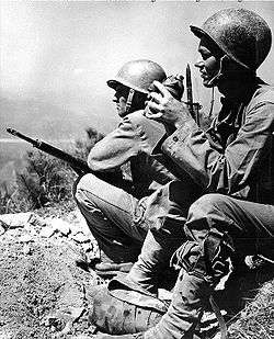 Two men in military uniforms sitting on a ledge overlooking a river