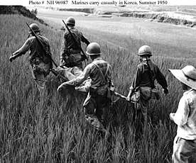 a group of men carry an injured man on a stretcher through a grass field