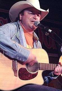 A man wearing a cowboy hat, playing a guitar and singing into a microphone
