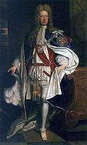 A man in robes of the Order of the Garter. The man is wearing white and red clothing, with a mantle adorned with a large badge