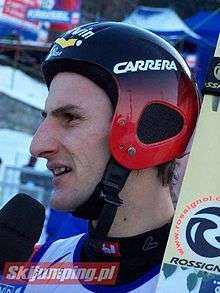 A man, wearing a ski helmet, talks into a microphone.