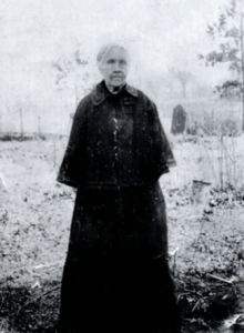 A grey-haired woman wearing all black, standing outdoors.