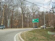 A road at a roundabout in a rural area with a sign to the left reading north Maryland Route 2 upper right arrow Maryland Route 408/Maryland Route 422 and a green sign to the right reading Maryland Route 2 north Annapolis straight