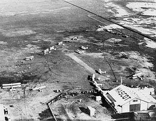 Airfield with several biplanes and hanger marked "MASCOT", photographed from overhead