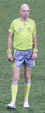 A man in a yellow shirt and shorts stands on grass