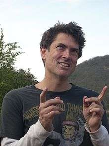 Smiling man outdoors, holding up both index fingers