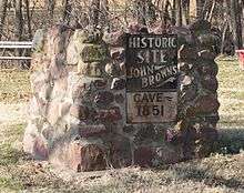 Metal sign on stone pier, reading "Historic Site – John Brown's Cave – 1851"