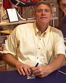 A man wearing a button-down shirt and signing something with his left hand