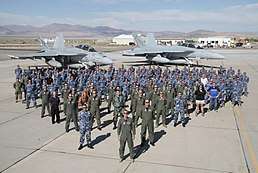 Colour photograph of a large number of people wearing military uniforms posing in front of two grey jet aircraft