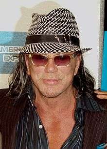 An image of a man with long hair in his 50's. He is wearing a hat and a dark shirt..