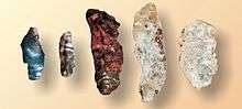 Five irregular but vaguely blade shaped pieces of crystalline rock. The left-most is blue, the next two are reddish, and the right two are white.
