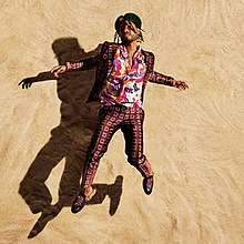 A man wearing a colorful shirt with dress clothes appears to be in the center of a sand wall background