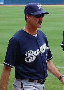 A thin, mustachioed man wearing a navy blue baseball cap and jersey