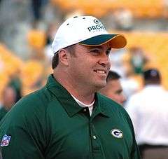 Candid photograph of McCarthy wearing a green Packers polo shirt and white Packers baseball cap