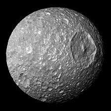 A spherical body is half illuminated from the left. The terminator runs from the top to bottom in the vicinity of the right limb. A large crater with a central peak sits on the terminator slightly to the right and above the center of the body. It makes the body look like the Death Star. There are numerous smaller craters.