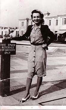 Black-and-white photograph of Stanhope smiling and standing, resting her right hand on a sign that reads in all-caps "THIS SPACE RESERVED FOR BATHERS ONLY"