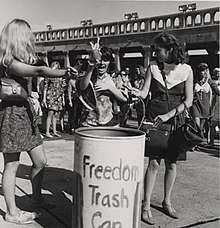 Women toss feminine items in a trash can as a form of protest about female sexualization and oppression