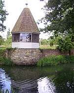 a summerhouse with a conical roof built on a stone wall above a moat
