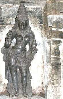 A stone carving of a standing woman with a pot in her left hand and lotus in right.