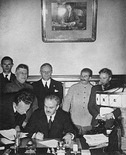 Soviet Foreign Minister Vyacheslav Molotov signs the Molotov–Ribbentrop Pact. Behind him stand German Foreign Minister Joachim von Ribbentrop and Soviet Premier Joseph Stalin.