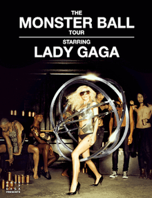 Gaga standing inside a series of metallic rings surrounding her. Few people are visible behind her, either standing or sitting down.