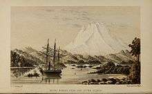 A white mountain rising over a forested bay with a ship