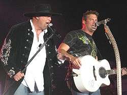 Eddie Montgomery and Troy Gentry of Montgomery Gentry singing into microphones, with Gentry also playing a white guitar