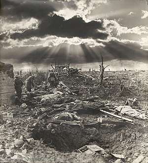 A sunburst through the clouds is shown against a landscape of destroyed land with a shellhole in the foreground.