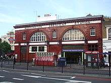 A red-bricked building with a rectangular, white sign reading "MORNINGTON CRESCENT STATION" in black letters all under a light blue sky