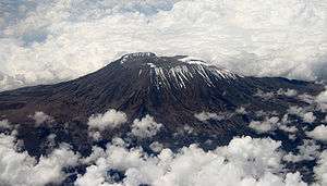 An aerial view of a large mountain's peak, encircled by many thick white clouds.