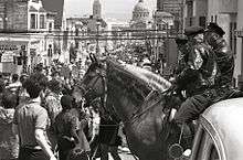 A pair of policemen mounted on horses observe a protest march down a street in San Francisco.