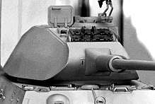 A tank turret with a front face which curves up and down. The sides are slanted vertically and curved laterally.