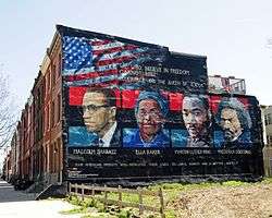 A painted mural shows the faces of Malcolm X, Ella Baker, Martin Luther King, and Frederick Douglass