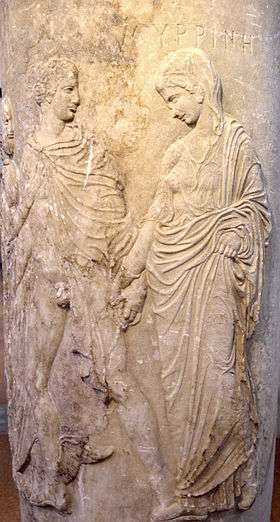 A carving of a noble robed man and woman apparently leading a demure, robed woman. The man's robe is open, exposing his penis. He holds the hand of the woman.