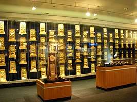 A room with glass display cases containing rectangular, wooden trophies that are gold-plated.