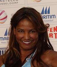 A woman with brown hair wearing a blue bikini top. She is smiling wide.