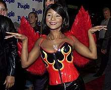An image of Natina Reed wearing red wings and a corset with flames. She is posing on a red carpet.