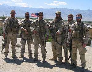A color image of six military personnel dressed in their combat uniforms and holding weapons.