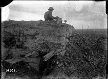 a man sitting atop a partially destroyed concrete bunker with a box in his hand.