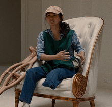 A Vietnamese woman wearing a cap and with her left leg missing below the knee sits in a chair with wooden crutches next to her.