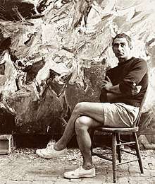 Nicolas Carone, sitting in his studio in East Hampton, NY, in the late 1950s, with one of his paintings behind him