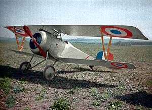 A white biplane fighter aircraft, with (in order of increasing size) blue, white and red concentric circles as the insignia on its wings, siting in a field of dirt