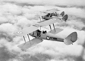 Rear three-quarter view of three biplanes in flight above clouds