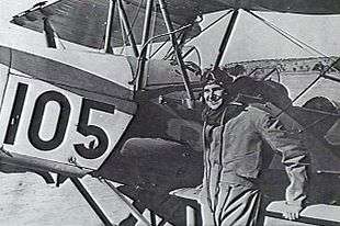 Pilot in flying gear next to biplane