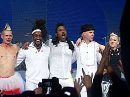 A color photograph of No Doubt posing together on stage after a performance.